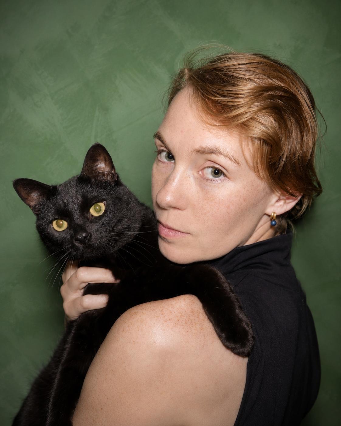 Ky Gerbush holding her black cat against a green backdrop